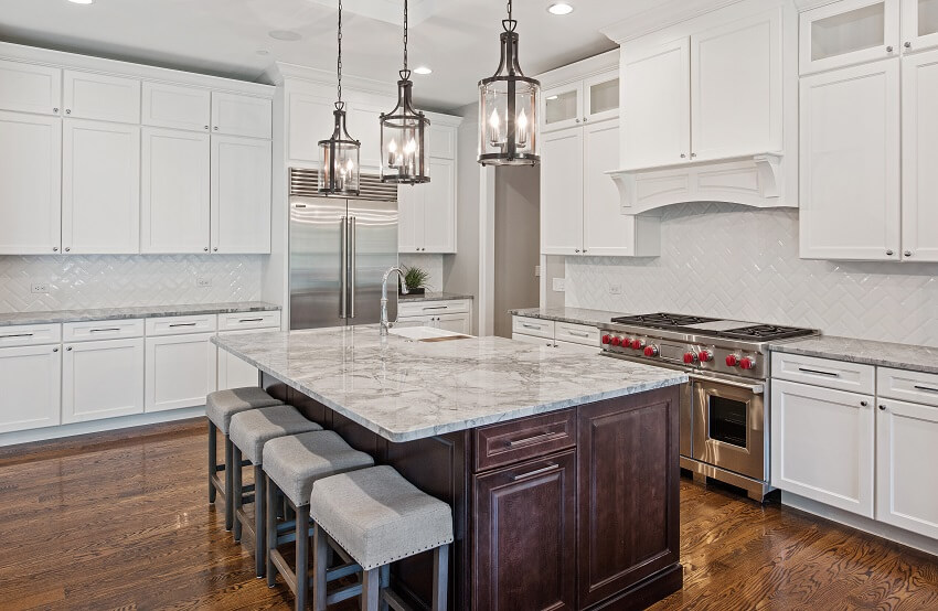 Empty kitchen with hardwood floors white cabinets stainless steel appliance brick tile backsplash and pendant lights hang above island with quartzite countertop