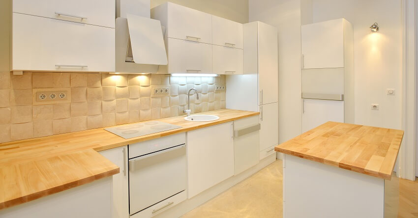 Empty kitchen with white cabinets wood countertops island adn white textured backsplash with sockets