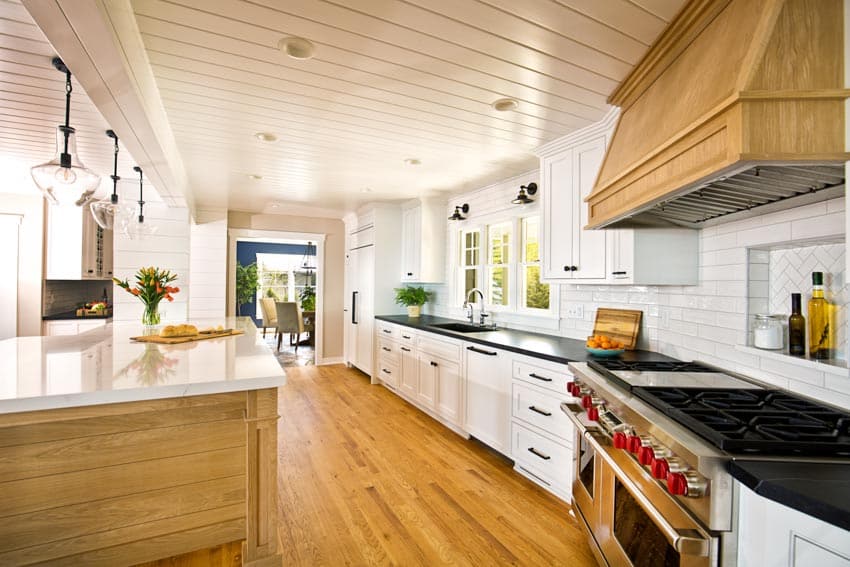 Modern farmhouse kitchen with marble and granite countertops wood floor shiplap ceiling hood hanging lights center island galley style windows
