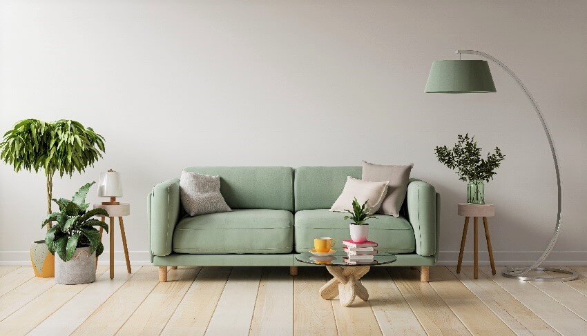 Green loveseat lampshade, plants, small table, empty wall and light floors in a modern apartment