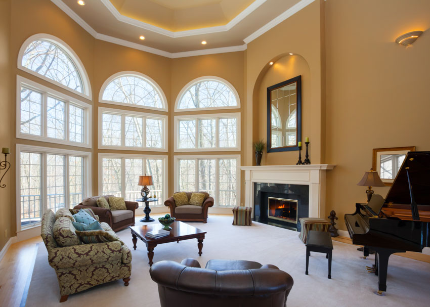High ceiling living room fireplace mantel piano sofa chairs furniture windows recessed lighting