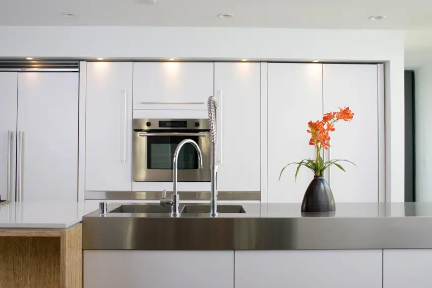 Kitchen counter made of metal, white glossy cabinets and sink