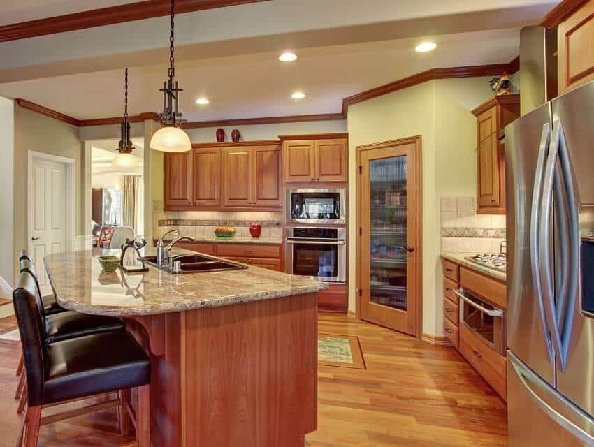 Kitchen interior with wooden cabinets bronzite countertop hardwood floor and island with bar stools sink and pendant light hung over