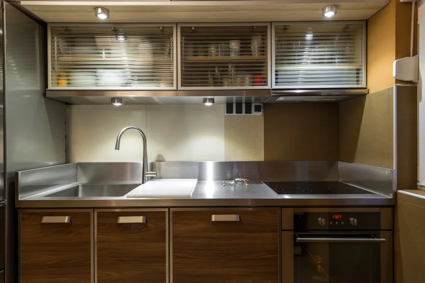 Kitchen with aluminum countertop sink wood and translucent cabinets oven lighting