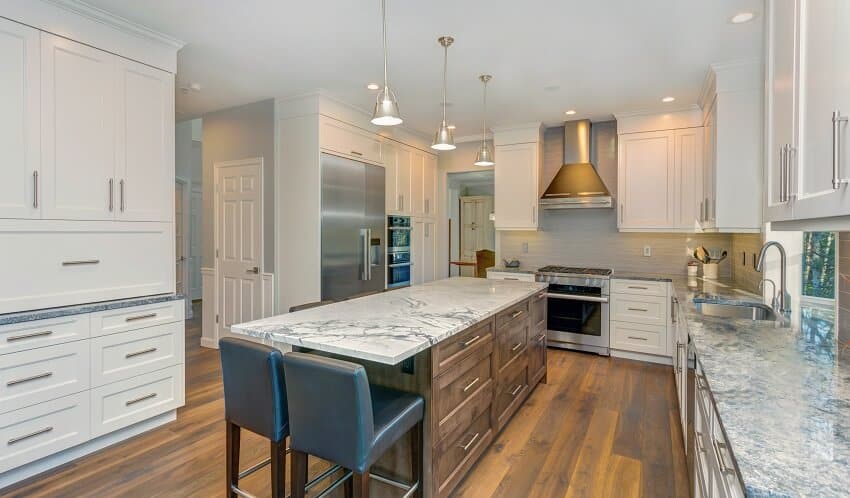 Kitchen with custom white shaker cabinets, long marble topped kitchen island with black leather stools over wide planked hardwood floor