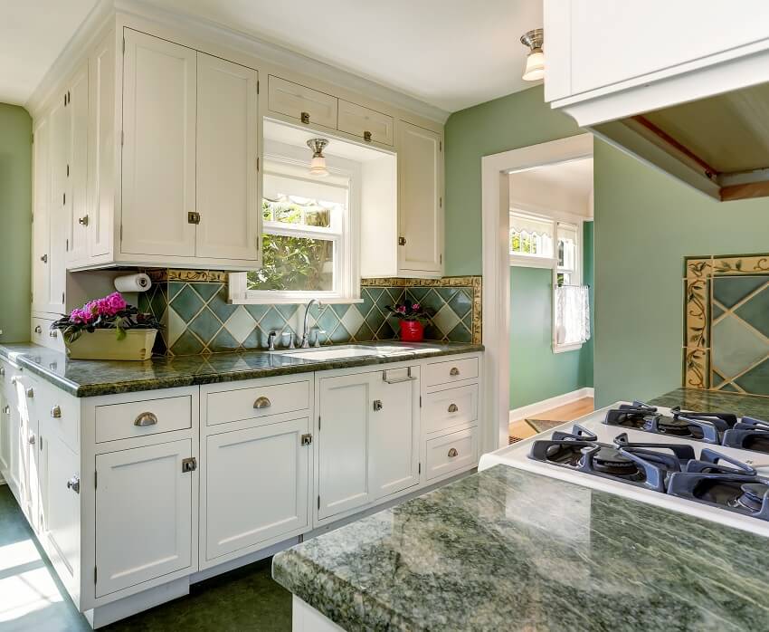 Kitchen with green walls white cabinets lighting fixtures flower decors on green countertops and backsplash in green and white tile