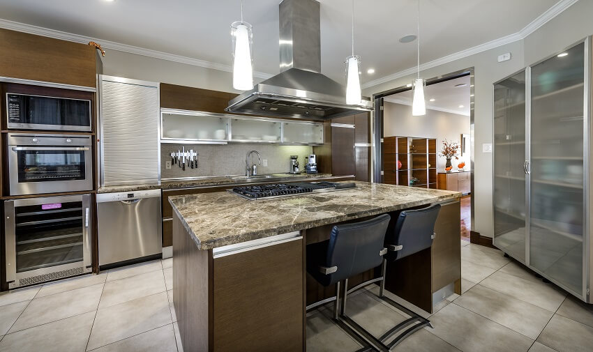 Kitchen with marble countertops flooring pendant lights stainless steel appliance and brown island with burner and exhaust hood