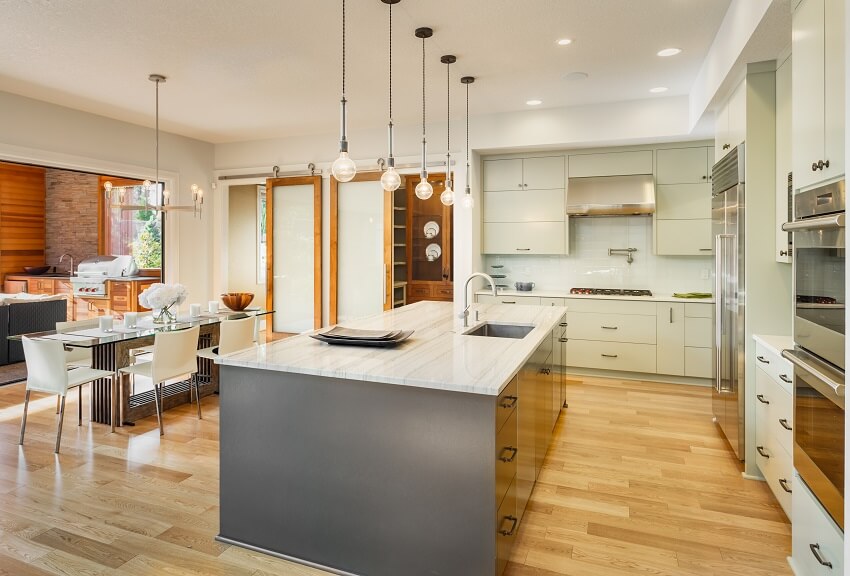Kitchen with stainless steel appliance small pendant lights tile backsplash hardwood floors island with mother of pearl countertop and view of the dining area