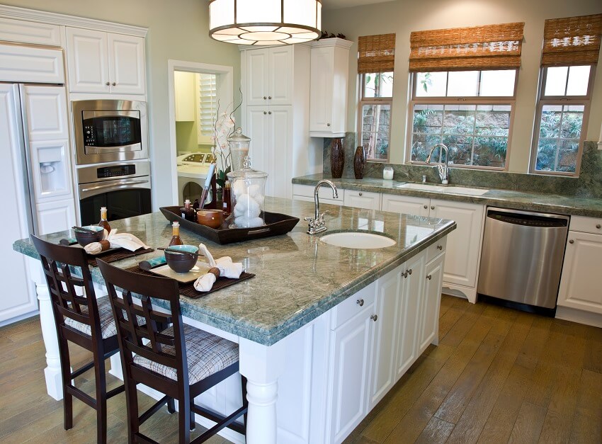 Kitchen with tray utensils and decors on island white cabinets window with brown shade stainless steel appliance wood floors and serpentine countertops and backsplash