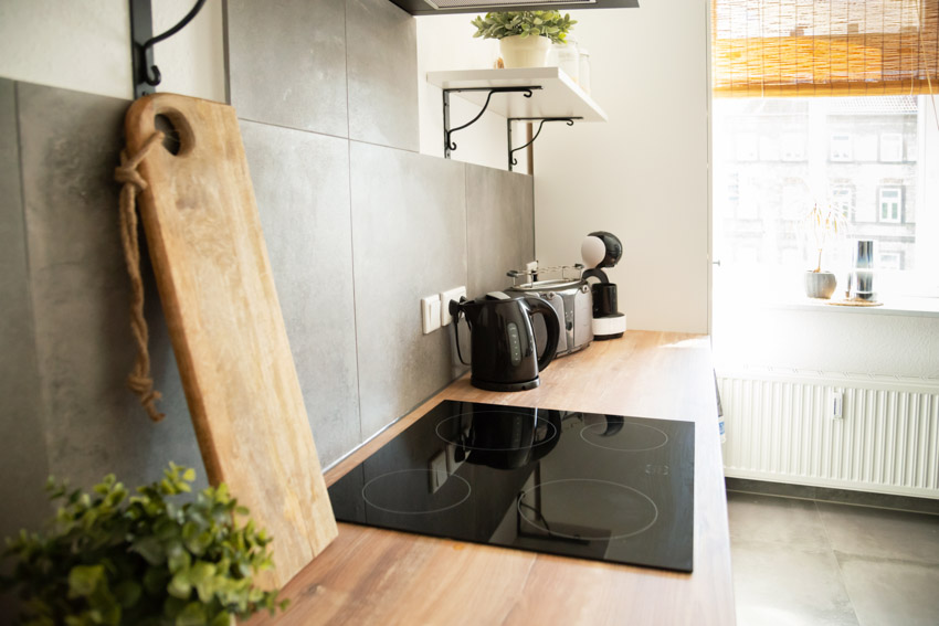 Kitchen wood countertop induction stove gray tile backsplash cutting board shelf