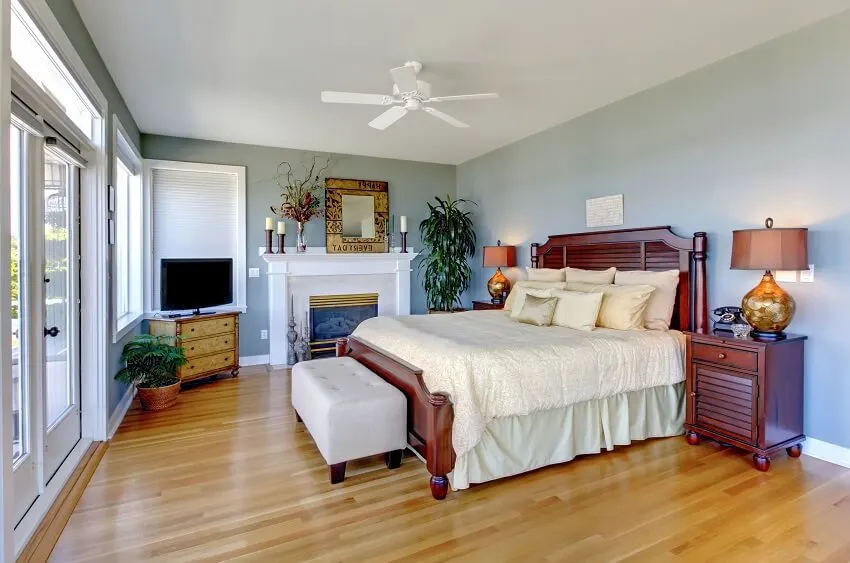 Large bedroom with fireplace green walls glossy wood floors wooden bed and furnitures tv indoor plants and a white ceiling fan