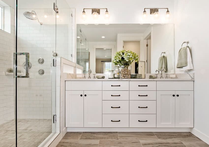 Large glass shower with brick wall tile flooring lighting fixture double sinks and two handle faucets in a bright bathroom