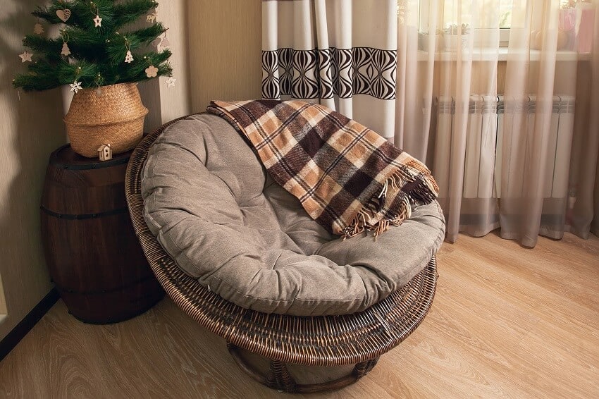 Round rattan chair with a warm plaid blanket and wood barrel table