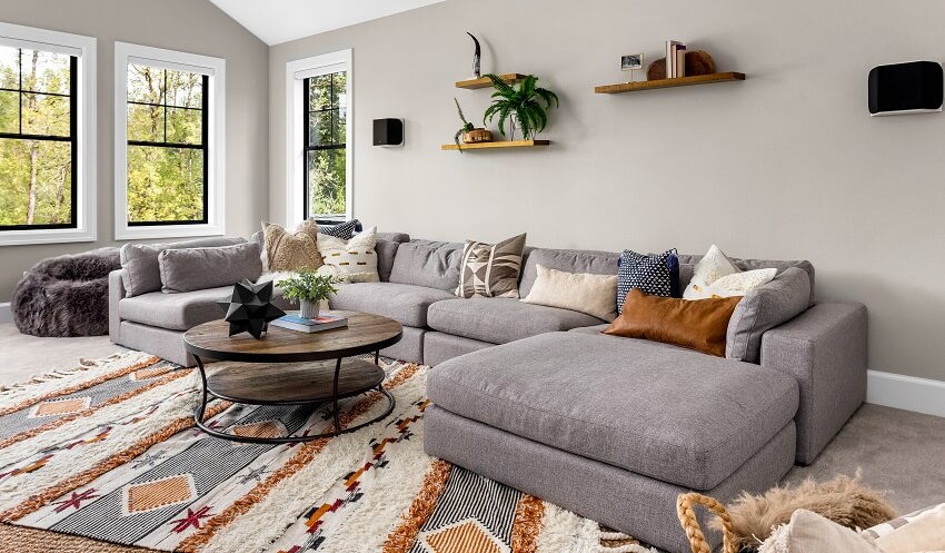 Room interior with colorful area rug, large couch, round table and open wood shelves with decor installed on a grey wall