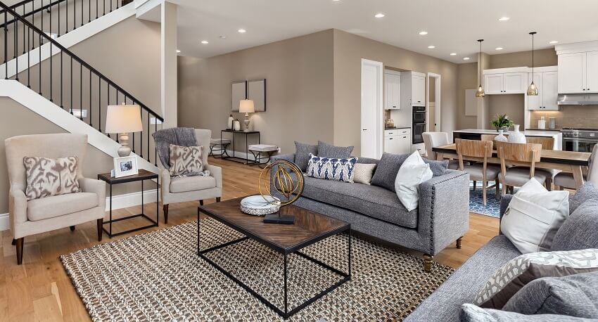 Room interior with hardwood floors, sofa, armchair, table, stairs with railings and view of kitchen and dining area