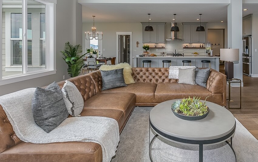 Room with brown leather couch with cushions, table and view of the dining area and kitchen with pendant lights, island and bar stools