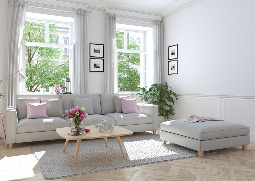 Room with natural light, mid century table, ottoman and grey sofa with cushions