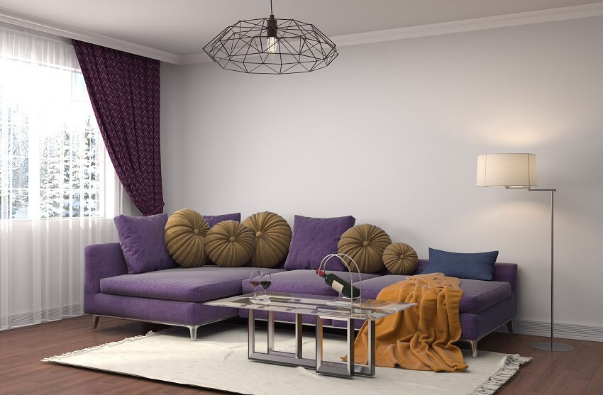 Living room with purple curtain and sofa brown cushions and blanket lighting fixures white carpet white walls and dark wood floors