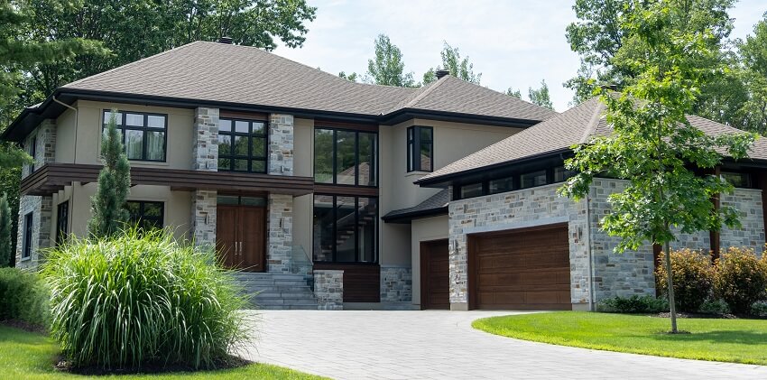 Luxury house with stone siding, columns, garage with wood doors, post and beam, wood double door entrance driveway, and green lawn