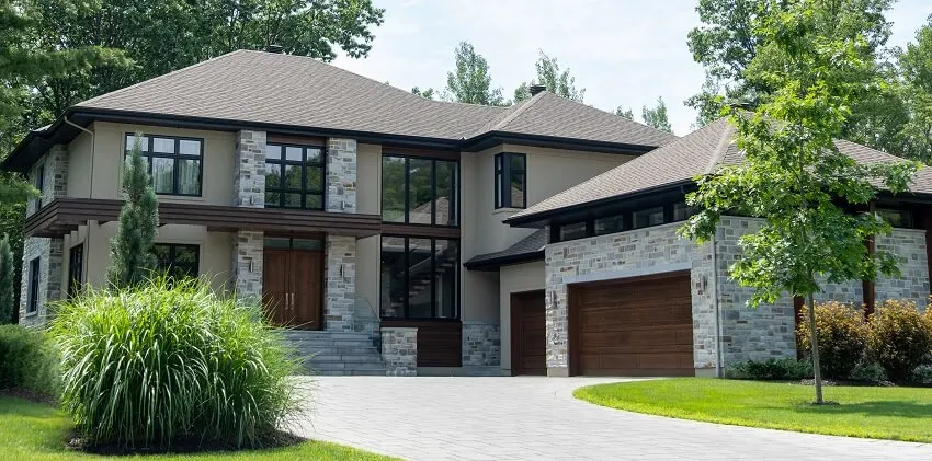 A house that has stone posts, garage with wood doors and double door entryway