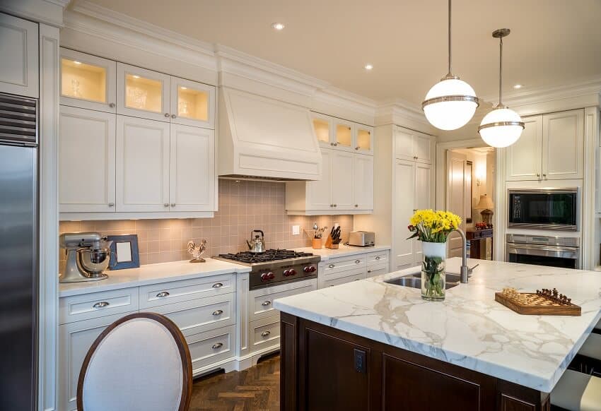 Luxury kitchen with pendants, white cabinets, wood floors, tile backsplash and island with honed stone countertops