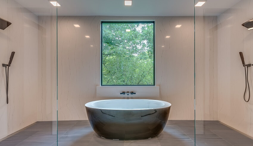 Luxury modern bathroom with freestanding tub showerheads on opposite sides a large window and grey tile floor