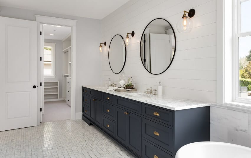 Master bathroom in luxury home with two sinks dark blue cabinets two round mirrors and view of the walk in closet