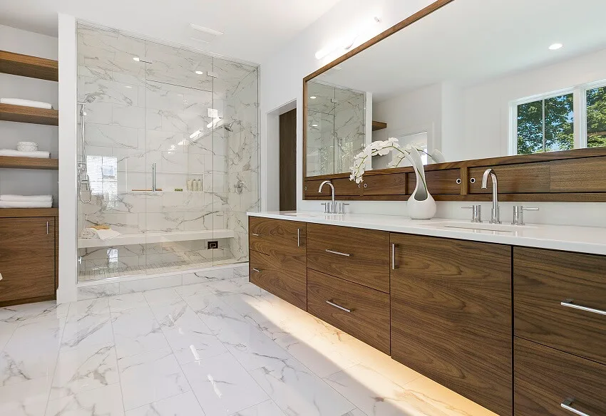 Mid-century modern look bathroom with large mirror marble tile wall and floor wood cabinets and shelves and a shower room with a bench