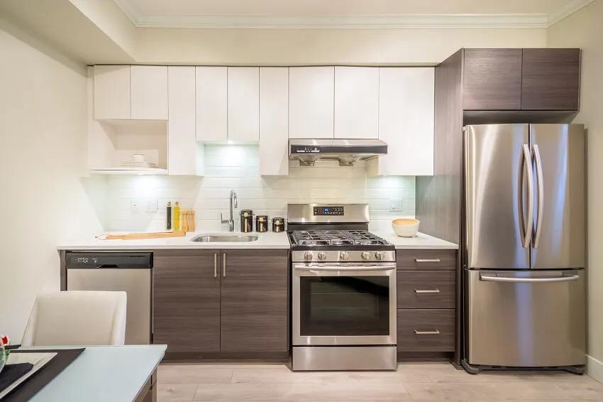 Modern bright kitchen with stainless steel appliance white tile backsplash brown and white cabinets and dining table with a white chair