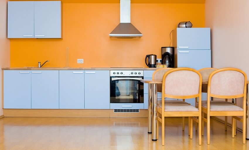 Modern fitted kitchen with blue cabinets orange and pink walls dining table with chairs and panel wood floors