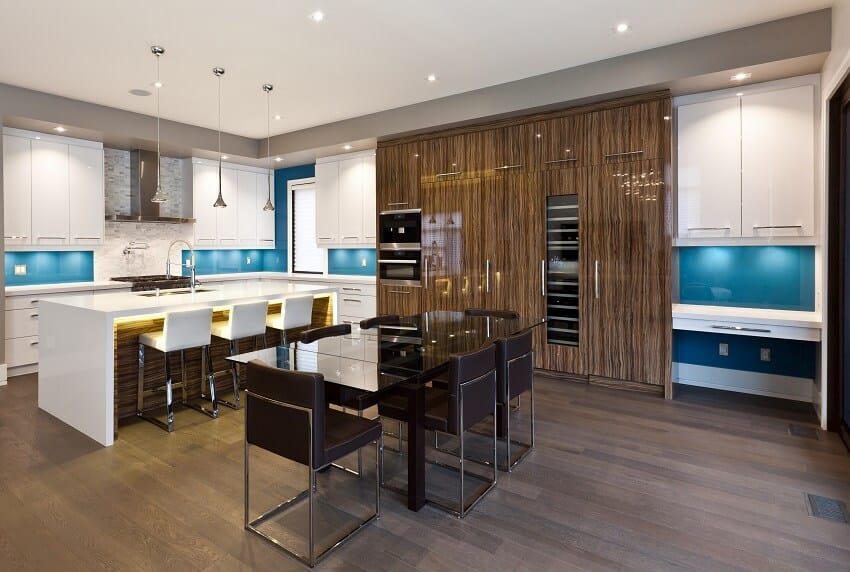 Modern kitchen and dining area with island with bar stools wood floors white countertops blue backsplash white and brown cabinets dining table and pendant lights