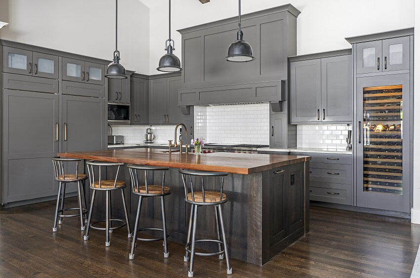 Modern kitchen with grey cabients, brick backsplash, wine storage, paneled floors and island with wood countertop and bar stools