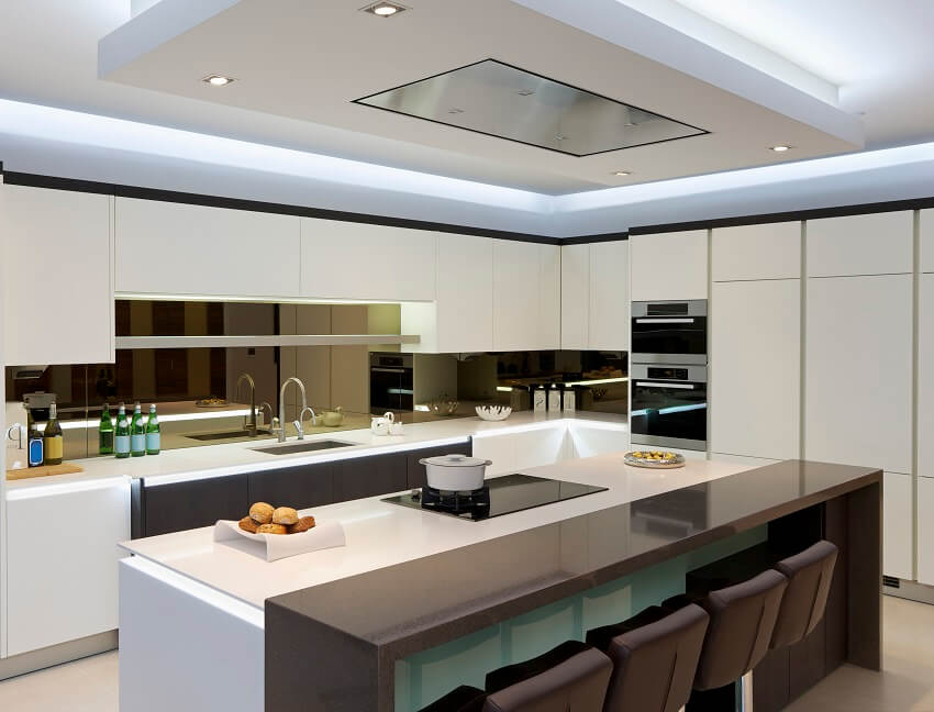 Modern kitchen with white cabinets, mirror glass backsplash and kitchen island with cooktop, barstools and brown granite breakfast counter