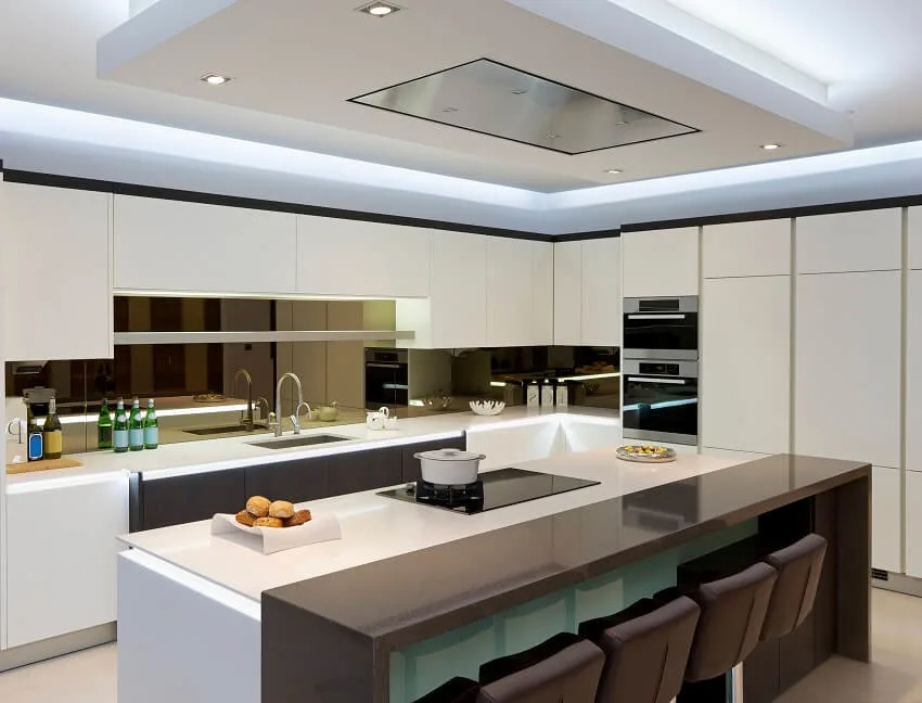 Modern kitchen with white cabinets, mirror glass backsplash and kitchen island with cooktop, barstools and brown granite breakfast counter