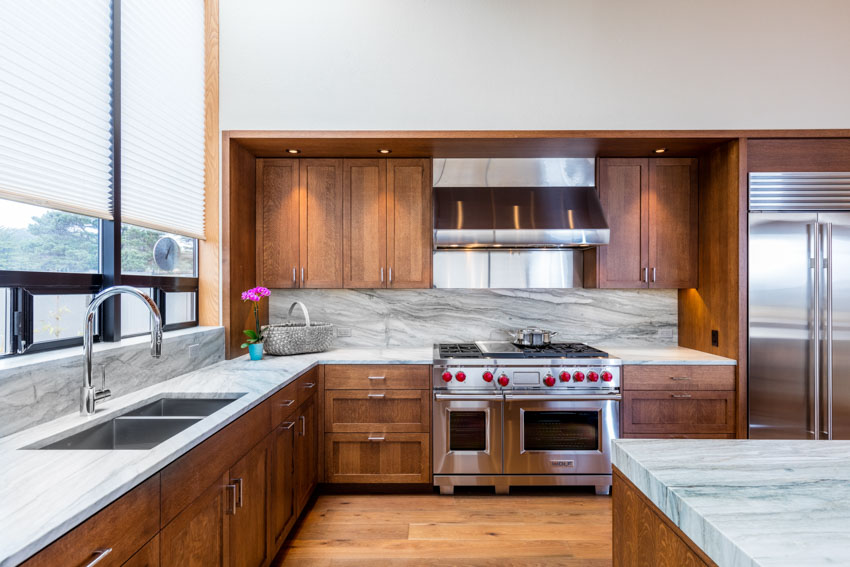 Kitchen with oak cabinets, drawers, marble countertop, center island, sink, windows, oven, and stainless steel hood