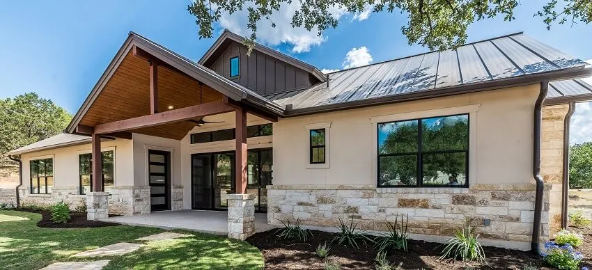 Mountain home exterior with stone wall trim glass doors metal roof post and beam in the porch and stone walkway 