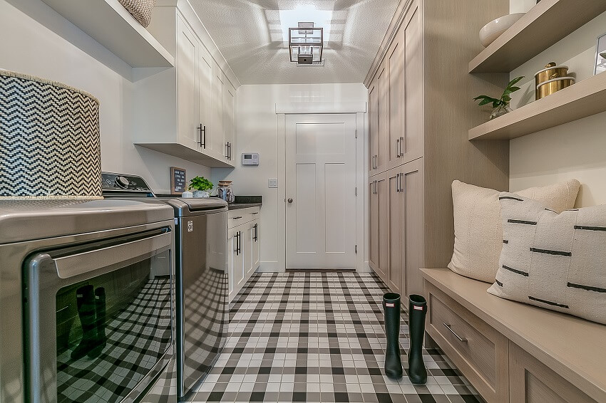 Mudroom and laundry room with connected cabinets shelves and bench with cushions appliances and boots on a gingham decorated flooring