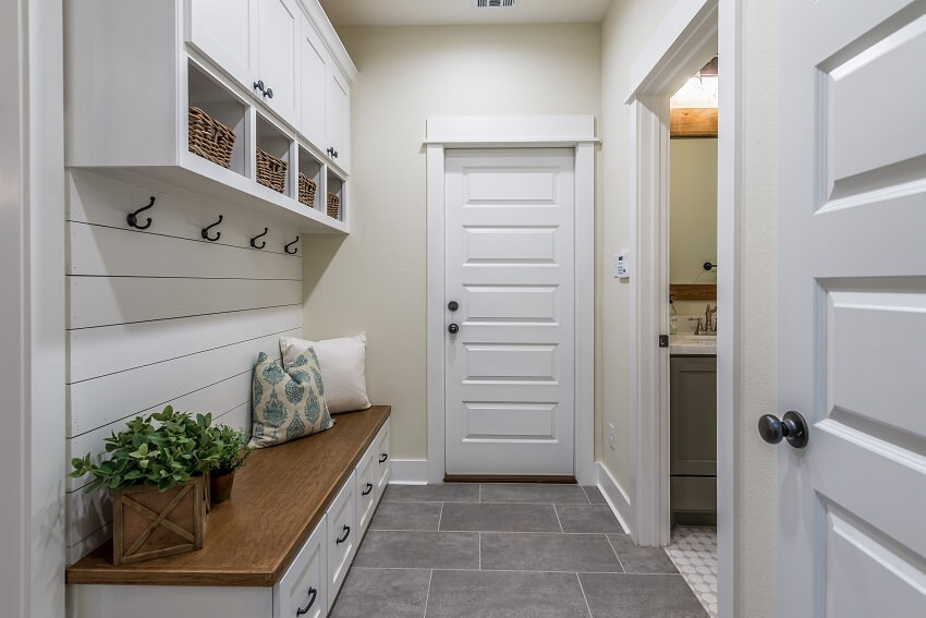 Mudroom with hooks installed to a white shiplap wall cabinets brown wood bench and grey tile flooring