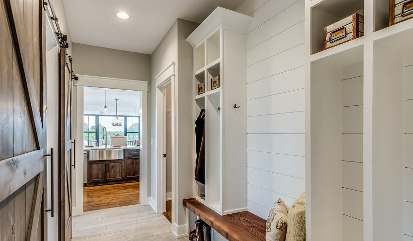 Mudroom with natural wood bench shiplap wall with a few cubbyhole lockers a wooden sliding doors and view of the kitchen