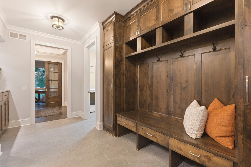 Natural dark wood mudroom with cushions on built in mud bench lighting fixture and tile flooring