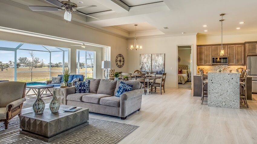 Open home interior with coffered ceiling, light lvf, kitchen island, dining table, grey sofa, and panoramic windows