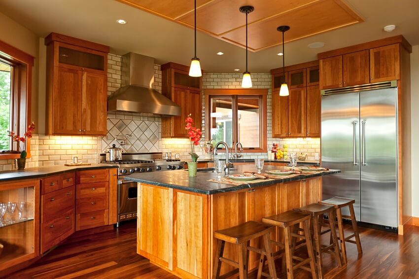 Open kitchen with walnut hardwood floors island with bar stools serpentine countertops brick backsplash pendant lights and wood cabinets
