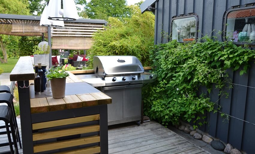 Outdoor kitchenette made with wood and metal with a stainless gas grill barstools and pendant lamps