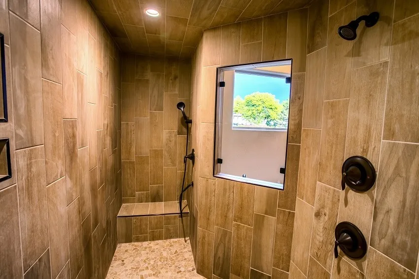 Residential bathroom with a bench mosaic tile floor window two showers and a wood like tile walls