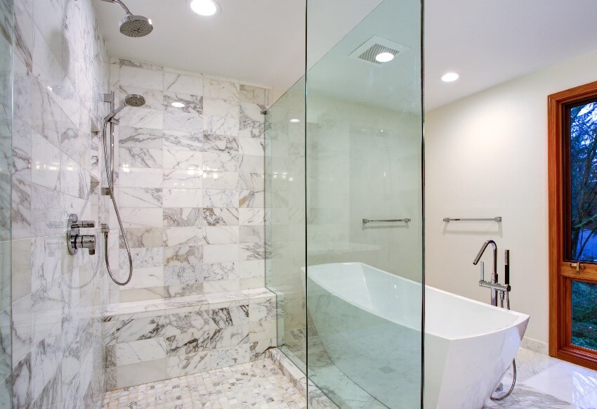 Sleek bathroom with freestanding bathtub paired with floor mounted faucet atop marble floor placed in front of glass shower with rain shower head and gray marble surround