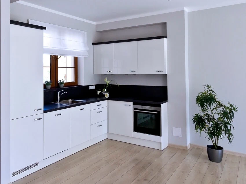 Small kitchen with white cabinets black countertops panel floors indoor plants and windows with white shades