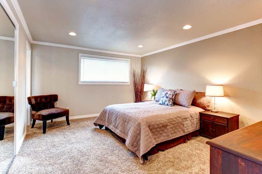 Spacious bedroom high pile carpet flooring window nightstand lamp chair low ceiling recessed lighting