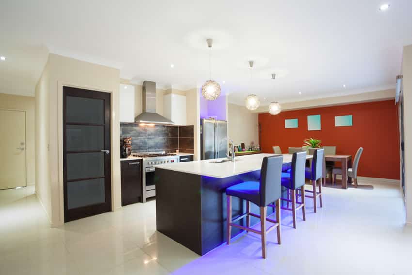 Spacious kitchen with red and white wall, ceramic floor and nanoglass top, below hanging lights