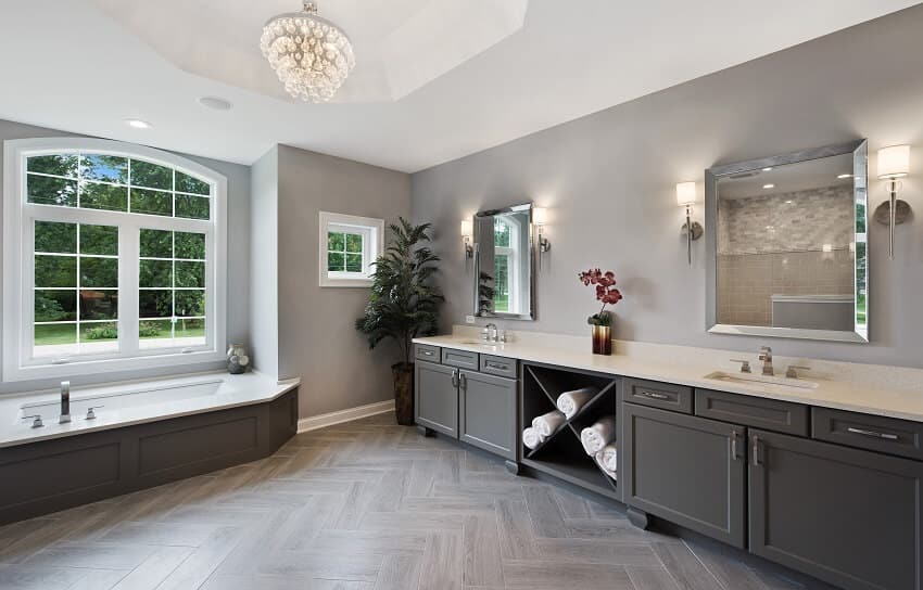Spacious master bathroom with windows chandelier bath tub sinks with under cabinets two mirrors and an indoor plant