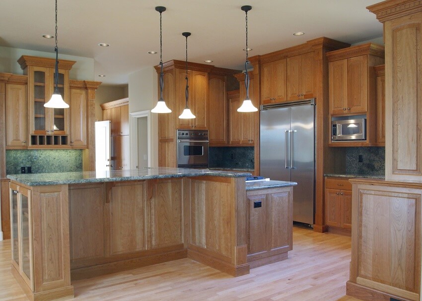 Spacious wood kitchen with stainless steel appliances pendant lights wood cabinets and serpentine countertops and backsplash